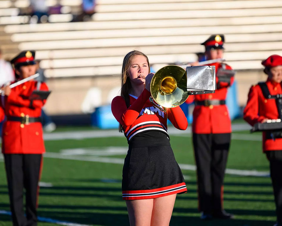 Marching band students on the field playing trumpet and flutes